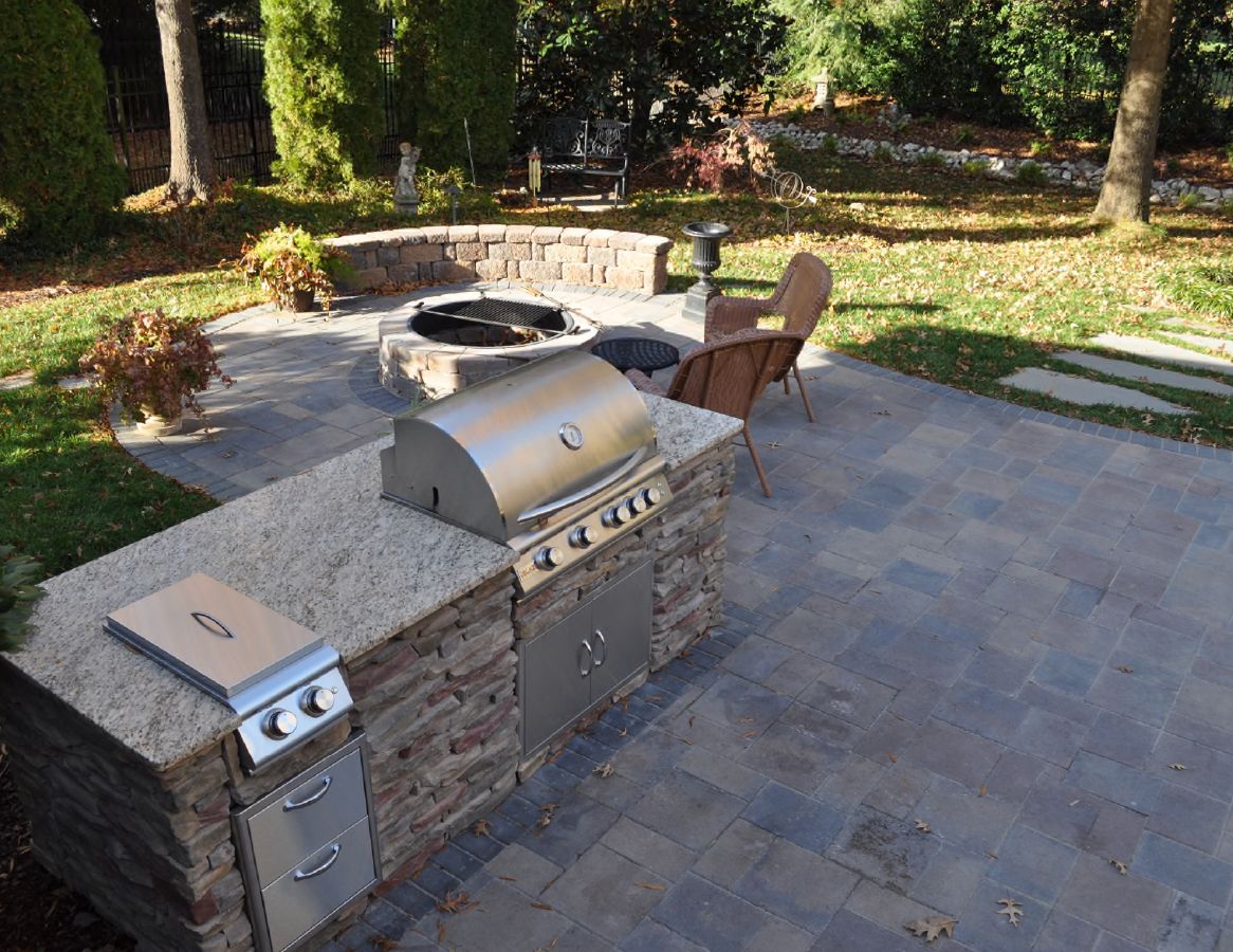 Paver patio featuring a seat wall, firepit, and custom outdoor kitchen by Archadeck of Charlotte.
